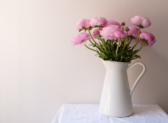 Fototapeta na wymiar Pink ranunculus flowers in white jug on small table