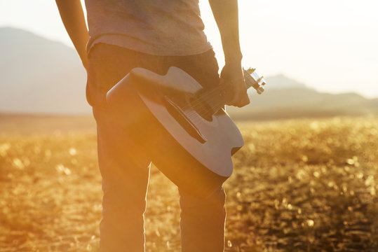 Closeup photo of man with guitar on sunset backdrop