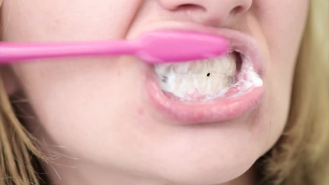 Close up portrait of woman cleaning her oral cavity caring about dental health. Pretty young female while brushing teeth in bathroom.