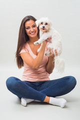 Cute little female maltese dog is looking at camera in arms of young beautiful woman.