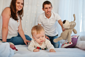 Mother and father with baby boy sitting on white bed with garlan