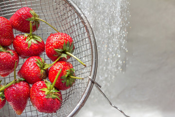 Red ripe strawberries in a stainless steel colander are rinsed u