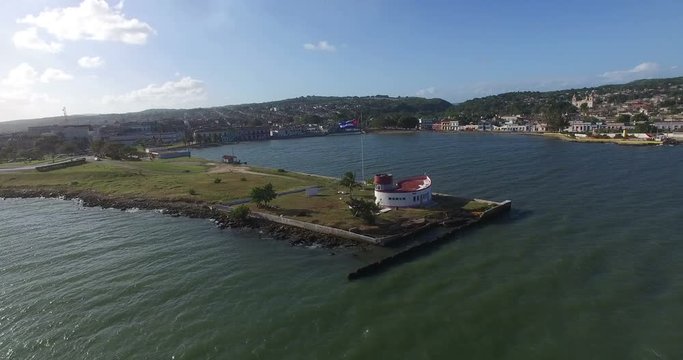 Bird's-eye view from drone to landscape of small peninsula, big building on the shore and fluttering down wind Cuban flag nerby.