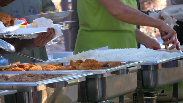 A line of people gather to get food on chaffing dishes at a catered Hawaiian party. HD 1080.