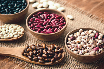 Beautiful multi-colored beans in bowls and wooden spoons on a background of burlap