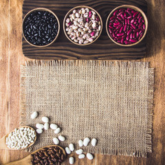 Beautiful multi-colored beans in bowls and wooden spoons on a background of burlap