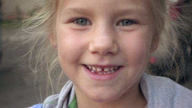 Close up of cute child with big smile and blue eyes looking into camera in slow motion. Portrait of laughing little girl enjoying happy childhood outdoors.