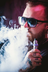 Men with beard  in sunglasses vaping and releases a cloud of vapor.