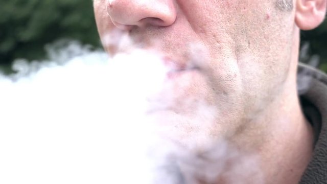 A man is exhaling the smoke cloud from his mouth in slow motion. E-cigarettes are the new sensation of smoking culture. Vapor does not need flame to start it.