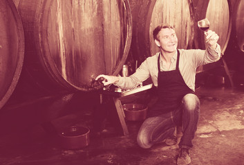 winemaker holding glass of wine in cellar.