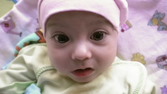Close up portrait of newborn baby with big brown eyes, looking around in slow motion. Surprised face of cute infant.