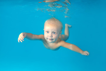 Fototapeta na wymiar Beautiful blue-eyed blond baby boy swims underwater on a blue water background. Healthy family lifestyle and children water sports activity. Child development, disease prevention