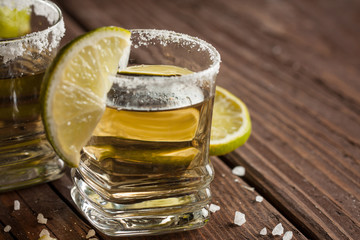 Macro focus photo of shots of golden Mexican tequila with lime and salt on wooden background. Alcoholic drink concept.
