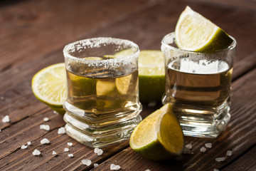 Macro focus photo of shots of golden Mexican tequila with lime and salt on wooden background. Alcoholic drink concept.