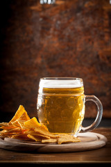 A glass of fresh cold light beer with nachos and wheat in a bar and a dark pub
