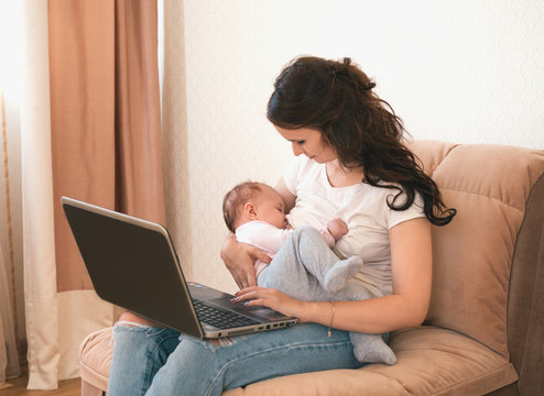 Beautiful young mother working with laptop computer and breastfeeding, holding and nursing her newborn baby at home. Mom - business woman.