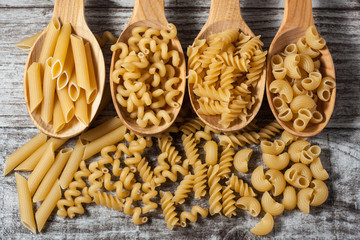Various mix of pasta on wooden rustic background, sack and wooden spoons. Diet and food concept.