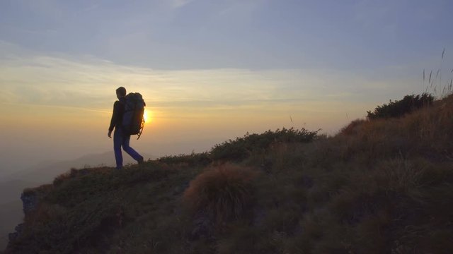 The man walk near the the cliff mountain on the background of sunset. Real time capture. Wide angle