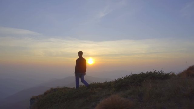 The man walk on the top of the mountain against the background of sunrise. Real time capture. Wide angle