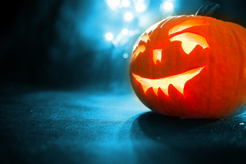 carved face of pumpkin glowing on Halloween on blue bokeh light background