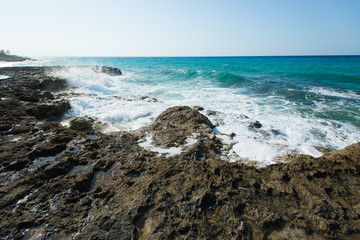 Fototapeta na wymiar High waves of the Caribbean Sea are splashing hardly against cliffs and rocks on a coastline at hot summer sunny day