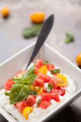 Cottage cheese with organic yellow and red tomatoes and basil on a metallic background