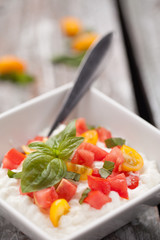 Cottage cheese with organic yellow and red tomatoes and basil in a square white bowl on a weathered barn wood table macro shot
