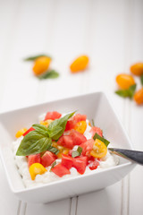 Cottage cheese with organic yellow and red tomatoes and basil vertical shot on white wood