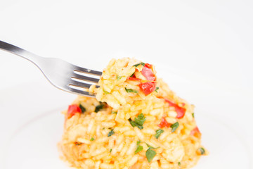 Risotto with chicken, tomatoes, bell pepper, onion and garlic on a white plate decorated with parsley being eaten with a fork