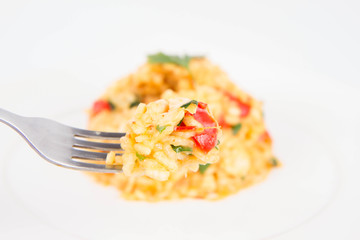Risotto with chicken, tomatoes, bell pepper, onion and garlic on a white plate decorated with parsley being eaten with a fork