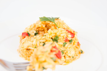 Risotto with chicken, tomatoes, bell pepper, onion and garlic on a white plate decorated with parsley being eaten with a fork
