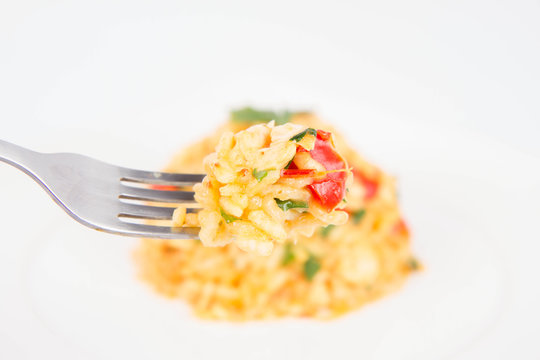 Risotto with chicken, tomatoes, bell pepper, onion and garlic on a white plate decorated with parsley being eaten with a fork