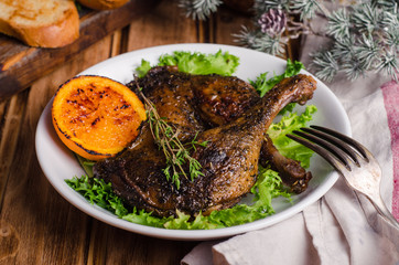 Confit duck legs with thyme and slice of orange in white plate on wooden background.  New year food. Selective focus