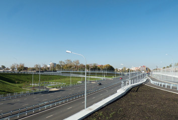Highway outgoing to the horizon with some cars. Sunny autumn day. High buildings in the background. City landscape with place for text (on the sky). Soft focus.