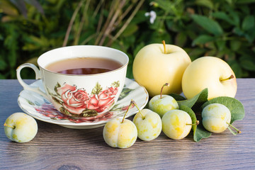 Obraz na płótnie Canvas Желтая слива, чашка чая и яблоки на деревянном столе
