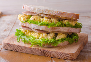 Sandwich with scramble eggs, leaves salad and ham on wooden baskgraund. Selective focus