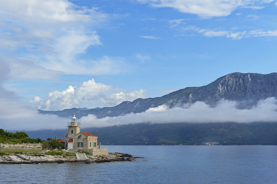 Leuchtturm an der Kueste mit Berg und Wolken