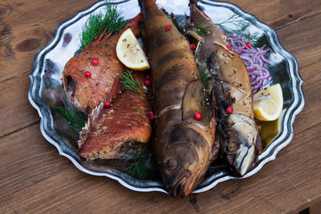 smoked fish mackerel, sea bass and lingcod on metal plate, wooden background