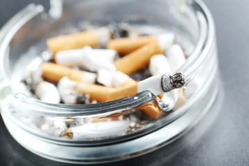 Cigarette butts with ash in ashtray on black background