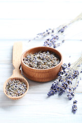 Lavender flowers in bowl and spoon on white wooden table