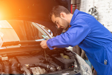 Young attractive mechanic working on a car at the garage - obrazy, fototapety, plakaty