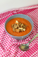 Gazpacho in a bowl with bread pieces on red checkered napkin. Vertical, selective focus. 