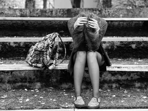 Woman sitting in despair on the bench in the park, head in the hands, black and white