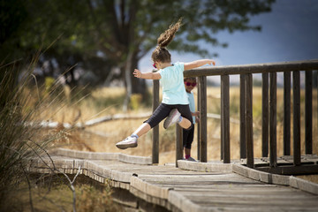 Fototapeta na wymiar Jovial kid jumping in mid-air on wooden path