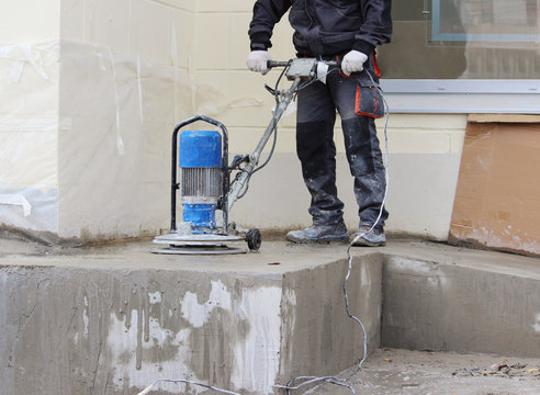 male worker works with the diamond grinding machine, polishing the porch in front of the office building. the cement floor  and construction .