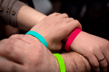 three hands of businesspeople on top of each other in colored wristbands