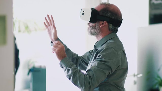 Mature business man wearing virtual reality googles / VR Glasses to work with in modern office