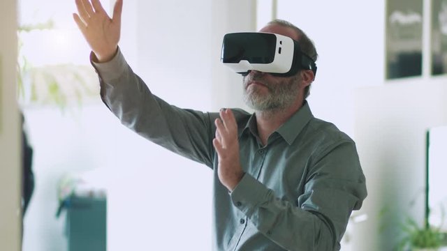 Mature business man wearing virtual reality googles / VR Glasses to work with in modern office