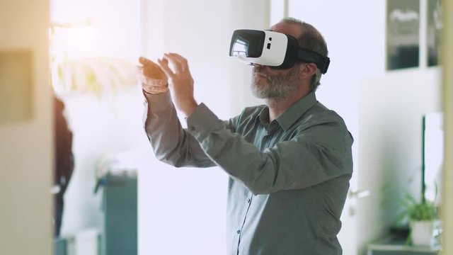 Mature business man wearing virtual reality googles / VR Glasses to work with in modern office