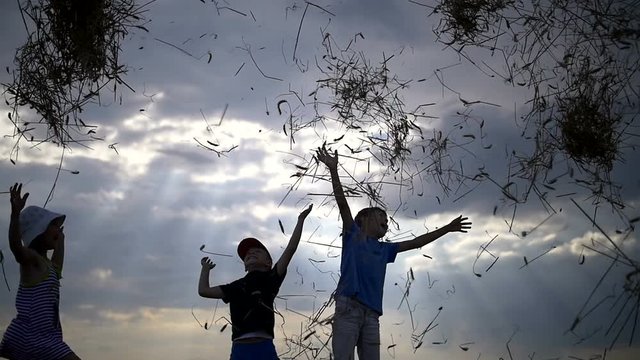 children throw up hay on a background of clouds at sunset, slow motion